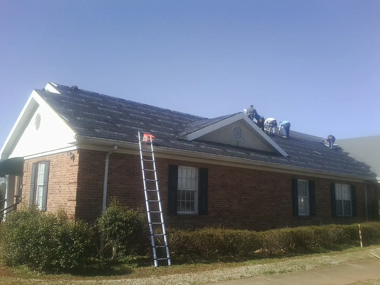 Crew tearing shingles off a brick ranch roof with a ladder set — Emergency Roof Repair work by our crew in Gardendale