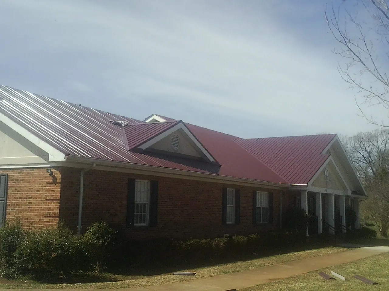 Red metal roof with gabled entries on a long brick building, from a Hail Damage Roof Repair job in Gardendale