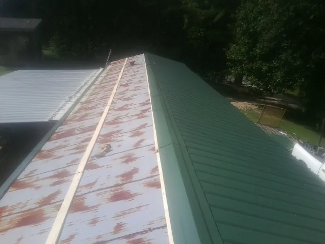 Old rusted panels beside newly installed green metal roofing — Wind Damage Roof Repair by Roofing Brothers in Gardendale