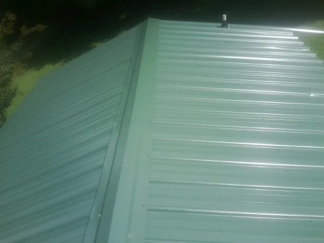 New green metal panels meeting at the ridge of a roof — Flat Roof Repair work by our crew in Gardendale
