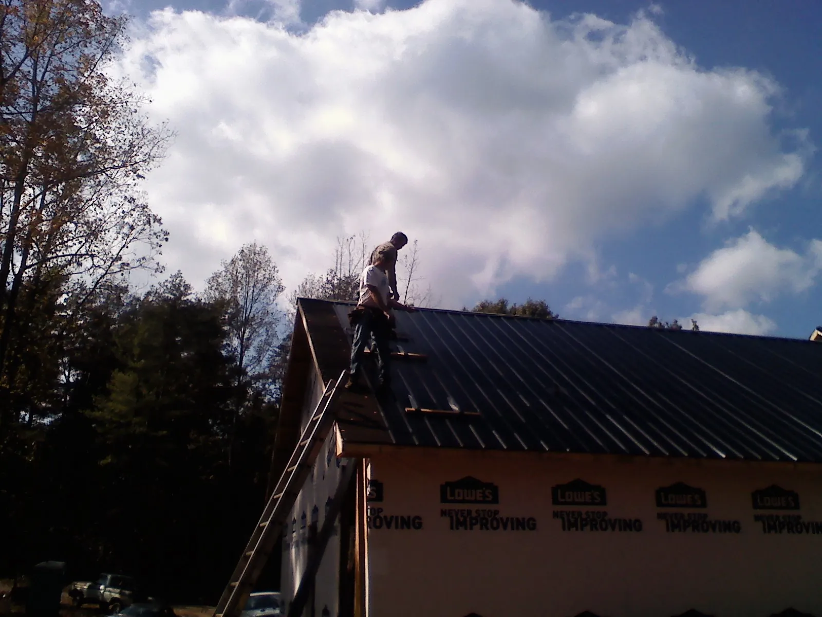 Roofer fastening dark metal panels high against a cloudy sky, from a Roof Inspection job in Gardendale