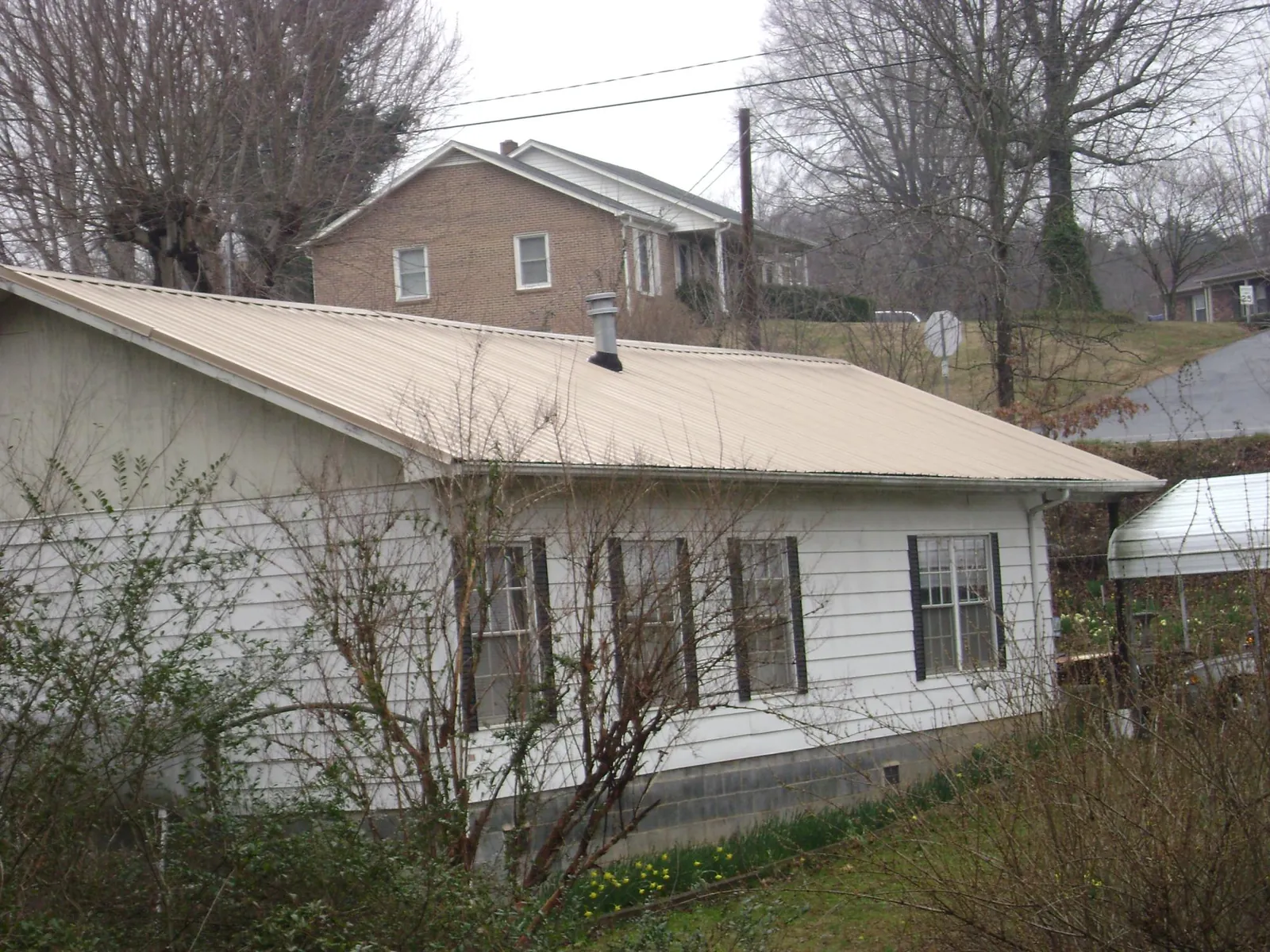 Tan metal roof on a white sided house set into a hillside — Commercial Roofing by Roofing Brothers in Gardendale