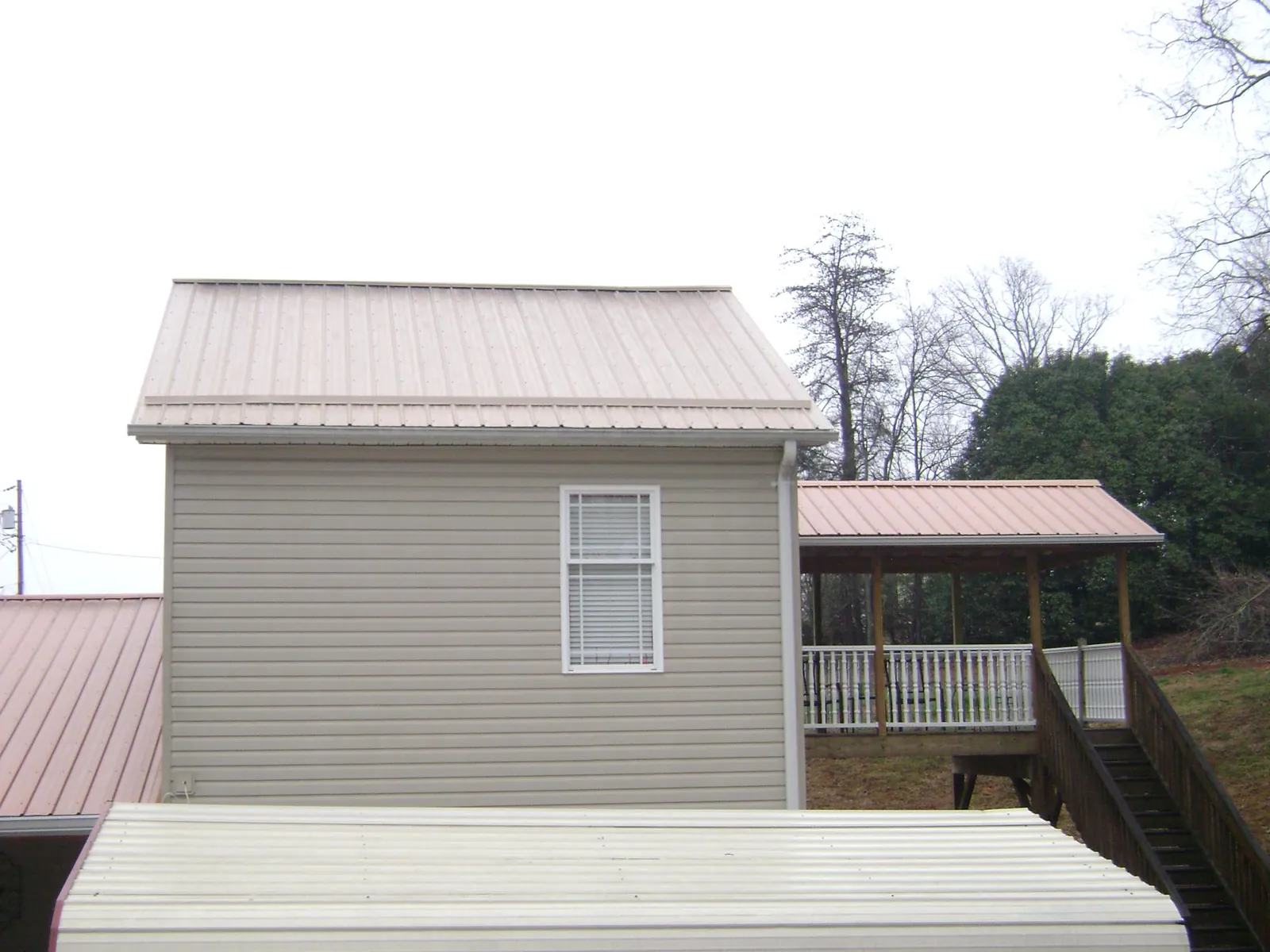 Tan metal roofs on a two story addition and attached porch, from a Roof Replacement job in Gardendale
